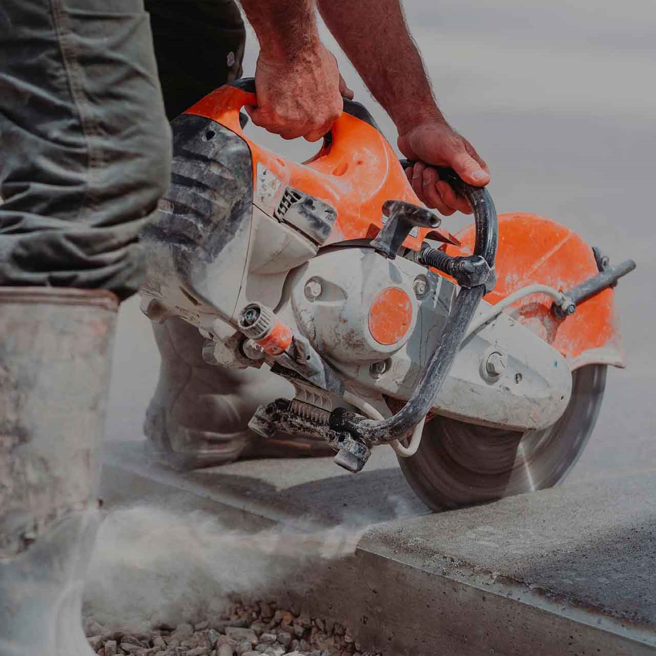 Utilisation d'une scie à béton au sol pour des travaux de construction, avec un homme effectuant une découpe précise.