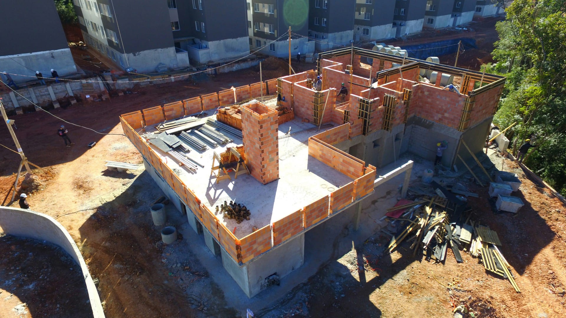 Chantier de construction en cours de redémarrage avec structure en briques, ouvriers au travail et équipements au sol.